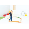 Moje Bambino Rollers Balance Board, a young child balancing on an orange and beige wooden balance board in a playroom with gym equipment.