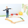 Moje Bambino Bases for Balance Boards, colorful child-friendly balancing board setup with a child standing on it and various exercise equipment in the background.