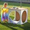 Whitney Brothers outdoorED™ Play House Cube, children outdoor playhouse with a colorful fabric and a wooden top, set outdoors on grass enclosed by a chain-link fence.