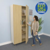 Whitney Brothers elevatED™ Tall and Wide Classroom Storage Cabinet, wooden cabinet with open door showing multiple shelves filled with classroom supplies, in a modern educational environment with a woman opening the cabinet, blue wall, and a potted plant nearby.