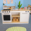 Whitney Brothers elevatED™ Kitchen Island Breakfast Bar, children's play kitchen with realistic stove, oven, sink, and storage compartments in a colorful playroom setting.