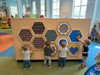 LiteZilla Multi-Sensory Hexagon Panel - Hex-A-Glow Classic, interactive sensory play panel with hexagonal sections featuring colorful LED lights and tactile activities for children in a play area.