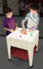 Childbrite Illumi Mite Light Table Kit Add On for Sensory Tables, children playing on illuminated sensory table with colorful translucent blocks in a classroom environment.