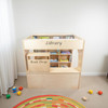 Wood Designs Town Collection Library Playhouse, a wooden children's library with labeled compartments for books and a built-in book drop, placed in a children's play area.