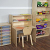 Wood Designs Contender Ready to Assemble Writing Desk, a light wood-colored compact desk with multiple shelves, a workspace surface, and a matching wooden chair, set in a children's playroom with toy storage and shelves.