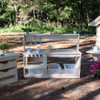 Wood Designs Kids Outdoor Kitchen, wooden outdoor play kitchen set with shelves, hooks, and storage bins, featuring colorful pots, cups, and gardening tools for children's imaginative play.