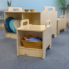 Whitney Brothers Stack-Able™ Seat, wooden modular children's seating with a basket of colorful fabrics inside, in a classroom setting.