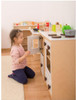 Moje Bambino Corner Play Kitchen, a young girl playing with a wooden toy kitchen set with stove, oven, and accessories.