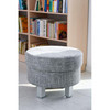 Moje Bambino Relax Round Ottoman, round upholstered footstool in light gray fabric in front of a bookshelf in a modern living room.