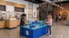 LiteZilla AeroCube Constructor Table - Blue, children arranging blue and white geometric construction cubes on a large interactive table in a science museum.
