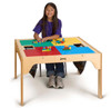 Jonti-Craft Wooden LEGO® Square Table With Dual Storage, a wooden educational table with Lego building bricks on its colorful surface and black mesh storage bins under the table.