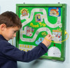 Playscapes Road Trip Magnetic Wall Activity, a child interacting with a green magnetic activity board featuring a colorful route map and various cityscape illustrations.