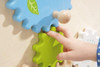 HABA Pro Grow.upp Gears Wheels Sensory Activity Wall Panel, child's hand interacting with green gear wheel and blue gear wheel, sensory developmental toy for children.