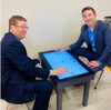 After Mouse Interactive Play Touch Table with Custom Company Logo, two men sitting and playing air hockey on a digital tabletop display.