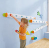 HABA Pro Marble Wall Track Catch Bin, child playing under marble track with wall-mounted catch bins in a playroom.