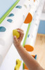 HABA Pro Marble Wall Track Catch Bin, child reaching to grab a yellow marble from the white marble track with colorful holes for playing and catching marbles