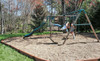 Frame It All Classic Sienna Curved Playground Border 16' - 2" Profile, brown curved horizontal border surrounding a playground area with swings and slide in a backyard.