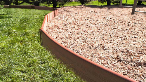 Frame It All Classic Sienna Curved Playground Border Kit 64' - 2" Profile, a curved plastic playground border kit installed around a mulch-filled play area with green grass and trees in the background.