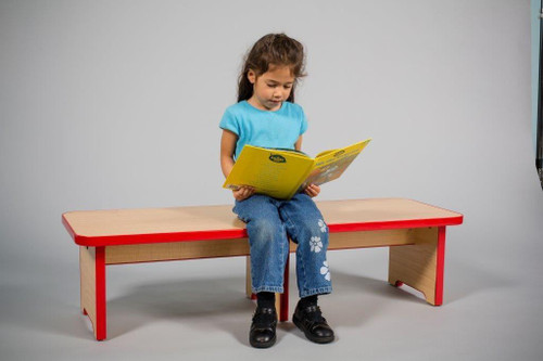 Playscapes School Time Bench, a wooden children's bench with a natural finish and red accents, on which a young girl in a blue shirt and jeans is sitting and reading a book.