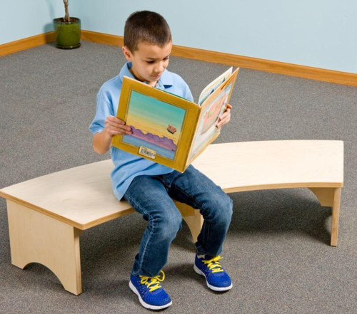 Playscapes Reading Retreat Bench, a child sitting on a curved wooden bench reading a book in a classroom setting.