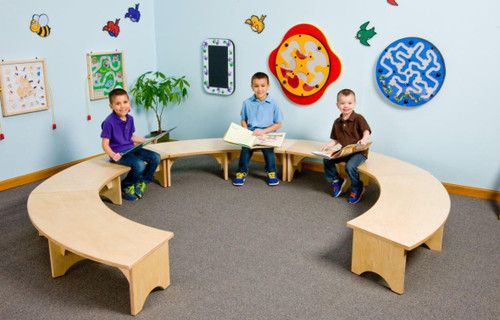 Playscapes Reading Retreat Bench, a semi-circular wooden reading bench with three children sitting and reading books in a colorful classroom with wall decorations.
