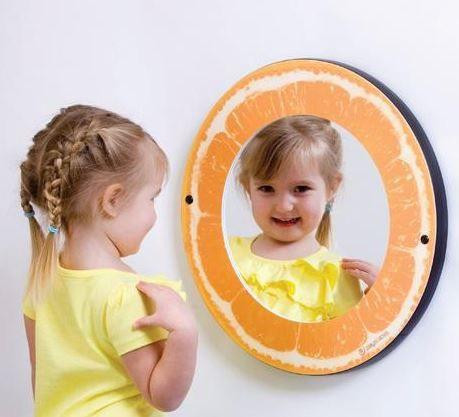 Playscapes Citrus Funhouse Mirrors - Choose from 3, a circular mirror designed to resemble an orange slice, reflecting a smiling girl in a yellow dress.