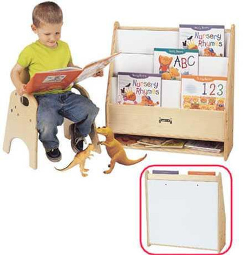 Jonti-Craft Toddler Pick-a-Book Stand, wooden book display with multiple slots holding children's books, small child reading a book and a small toy dog beside him.