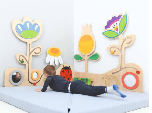 Moje Bambino Meadow with Ladybug Sensory Wall Panel, colorful wooden children's sensory wall with flower, ladybug, and ladybird designs, situated on a padded play area.