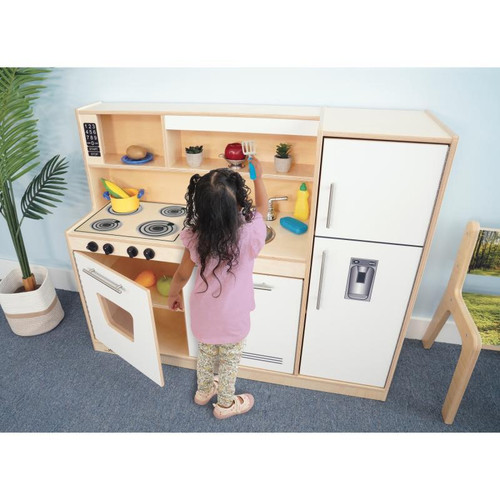 Whitney Brothers Contemporary White Play Kitchen Combo, a child playing with a pretend kitchen set that includes a stove, sink, refrigerator, and storage compartments.