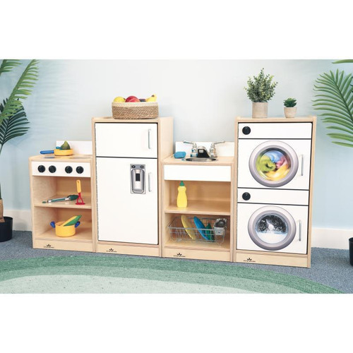 Whitney Brothers Let's Play Toddler Kitchen Play Set - White, child-sized wooden play kitchen with stove, sink, washer and dryer units, and storage shelves, decorated with potted plants and toys.