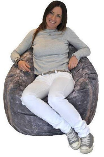 Playscapes Woodsmen Naturescape Stone Pod, a woman sitting on a large, round, stone-textured bean bag chair, smiling and relaxed.