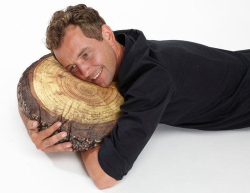 Playscapes Woodsmen Naturescape Annual Rings Log Slice Cushion 15¾", man lying on the log-shaped cushion with a big smile, showcasing the natural wood pattern and rings.