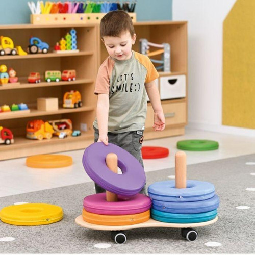 Moje Bambino Mobile Trolley with Donut Seating Cushions Set, a boy is stacking colorful donut-shaped cushions on a mobile trolley in a playroom with toy cars and accessible storage shelves.