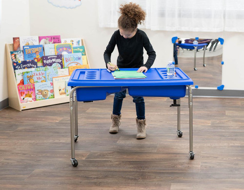 Children's Factory Neptune Sensory Table and Lid Set - 24 inches high, blue sensory table with girl writing in a classroom setting.