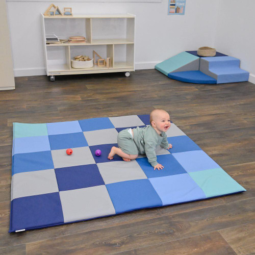 Children's Factory Patchwork Activity Play Mat, Tranquility, with a baby crawling on it, in a child-friendly room.