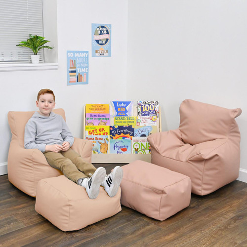 Children's Factory Cozy Soft Chair and Ottoman - Almond, soft pink kids' chair and ottoman in a cozy reading nook with a boy sitting on the chair, in a child-friendly room with interactive posters and a bookshelf of children's books.