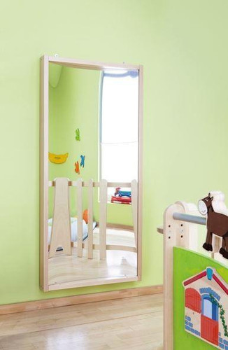 HABA Pro Concave Fun House Curved Mirror, a large, child-friendly mirror with a curved shape, mounted on a wall in a brightly colored children's playroom.