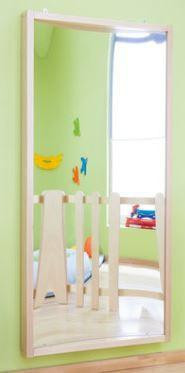 HABA Pro Concave Fun House Curved Mirror, reflective mirror with wooden frame in a children's playroom with bright green wall and colorful decorations.