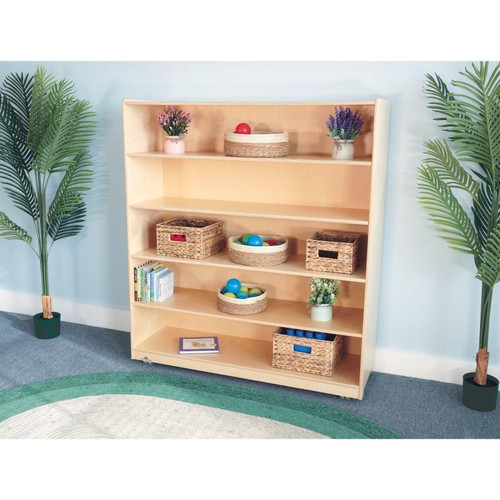 Whitney Brothers Mobile Bookshelf Cabinet 54H, light wood-colored storage unit with multiple shelves containing baskets, books, and decorative items, flanked by green potted plants in a cozy room.