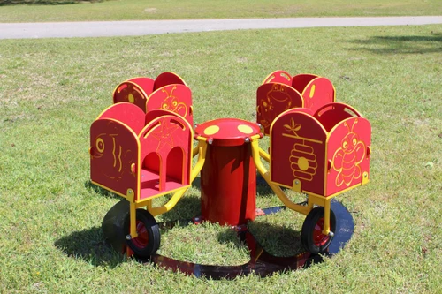 Infinity Playgrounds Carrington's Carousel Toddler Easy Rider Merry Go Round, colorful red and yellow toddler merry go round with bug, starfish, and sea creature designs on the side panels in a park setting.