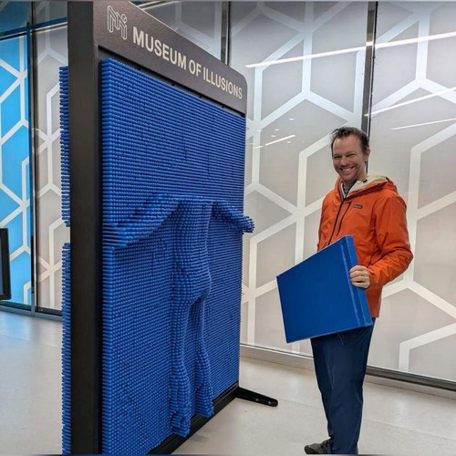 LiteZilla Clone Box Giant Pin Wall STEM Activity, interactive blue pin wall with a person holding a blue panel demonstrating the pin wall at the Museum of Illusions.