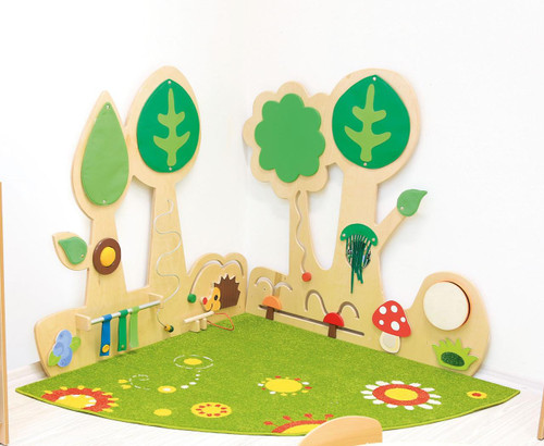 Moje Bambino Meadow Corner Carpet, a children's play corner with a green grassy carpet and wooden wall decor shaped like trees, flowers, and insects.