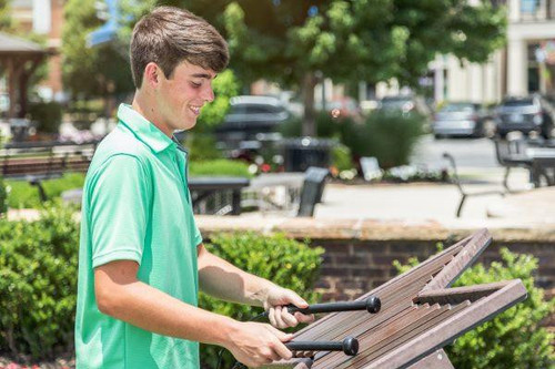 Freenotes Cadence Outdoor Marimba, a young man playing a large wooden outdoor marimba in a park setting.