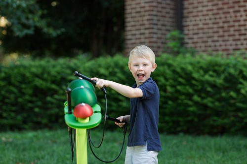 Freenotes Caterpillar Bells, a musical outdoor instrument for children, with a green caterpillar-shaped design played by a joyful young boy outside in a grassy yard.