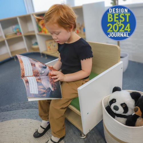 Whitney Brothers elevatED Children's Arm Chair, a wooden child's arm chair with a green seat, used by a young girl reading a book in a classroom setting.