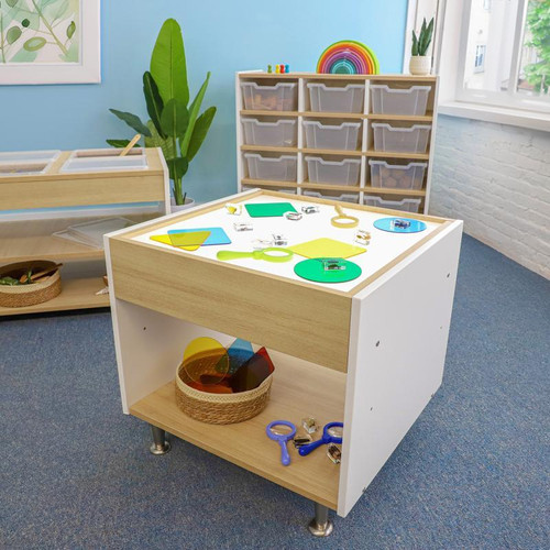 Whitney Brothers elevatED™ Adjustable Light Table, children’s art and activity table with illuminated surface, on a classroom floor with educational materials and storage bins in the background.