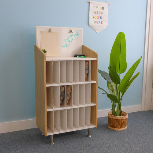 Whitney Brothers elevatED™ Mail And Message Center, a compact wooden organizational unit with multiple labeled mail slots and a whiteboard on top, placed next to a green potted plant in a modern indoor setting.