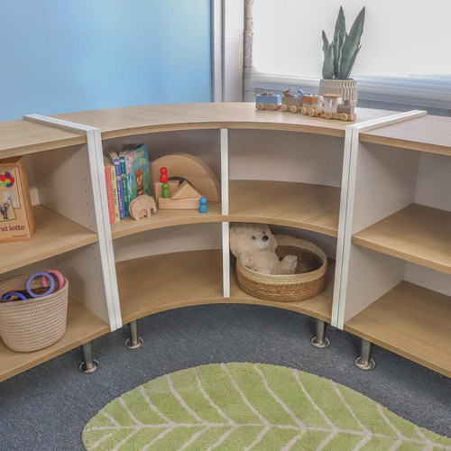 Whitney Brothers elevatED™ Curve Out Cabinet 27"H, wooden curved storage cabinet with open shelves, toys, and a plush teddy bear in a child’s playroom.