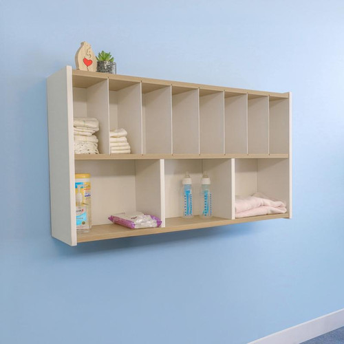 Whitney Brothers elevatED™ Wall Mount Diaper Supplies Organizer, wooden wall-mounted storage unit with multiple compartments for baby diapers, bottles, and supplies, mounted on a light blue wall.