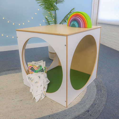 Whitney Brothers elevatED™ Play House Cube With Floor Mat Set, a colorful wooden playhouse cube with circular openings and a green floor mat, featuring rainbow stacking arches on top, in a children's playroom.